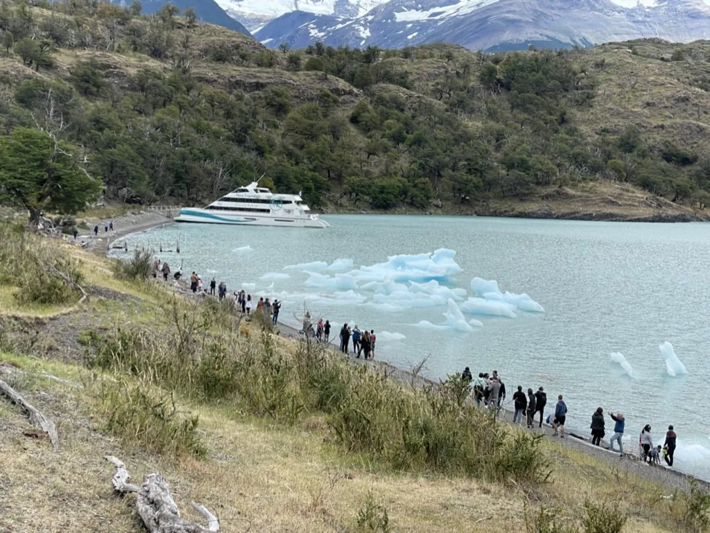 Travelers walking beside a Patagonian lake filled with icebergs